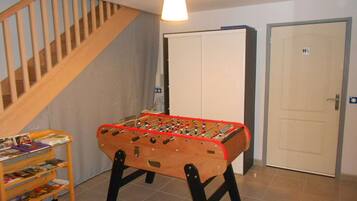 Een kamer met een tafelvoetbalspel, een boekenkast, een trap en een deur.