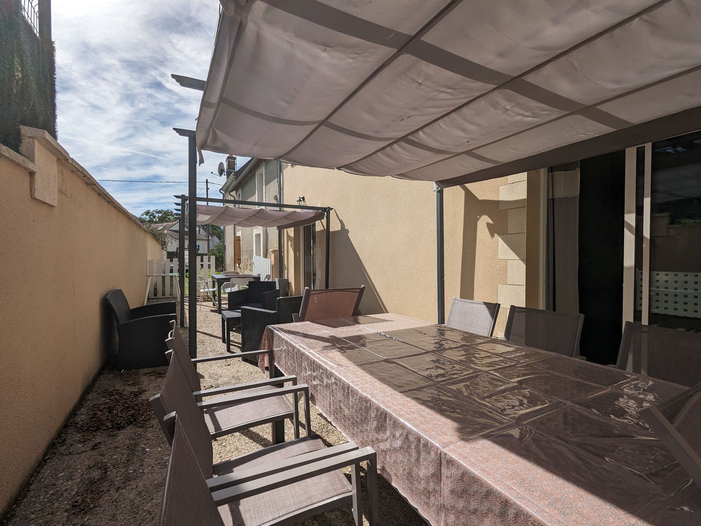 An outdoor patio with a covered table and chairs, a pergola, and a view of neighboring houses.