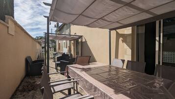 An outdoor patio with a covered table and chairs, a pergola, and a view of neighboring houses.