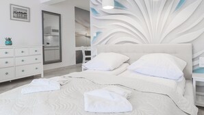 A modern bedroom with a large bed, white bedding, a decorative wall panel, a dresser with drawers, and a mirror. - Morski Anioł by Baltic Home (Swinoujscie)