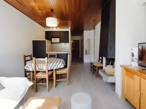 A cozy room with a wooden ceiling, a dining table with chairs, a sofa, a TV, and a fireplace.