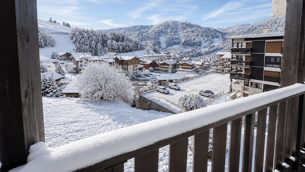 Un pueblo de montaña nevado con edificios, un estacionamiento y vistas de colinas cubiertas de nieve.