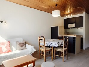 A compact living space with a sofa, dining table, chairs, a kitchen area with a microwave, and a ceiling light fixture.
