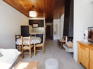 A cozy room with a wooden ceiling, a dining table with chairs, a sofa, a TV, and a fireplace.