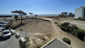 A parking area with several cars, a pathway leading to a beach, and a building with a flat roof. - Saint-Cyprien: Cozy seafront T2 with parking and pets allowed (Saint-Cyprien)