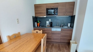 Cocina compacta con armarios de madera, microondas, lavaplatos y una mesa de comedor con sillas.