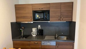 Una cocina compacta con armarios de madera, un microondas, una cafetera y un lavavajillas.