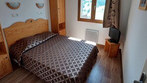 Un dormitorio con cama de madera, televisor sobre un mueble de madera, ventana con vista a un bosque y armario.