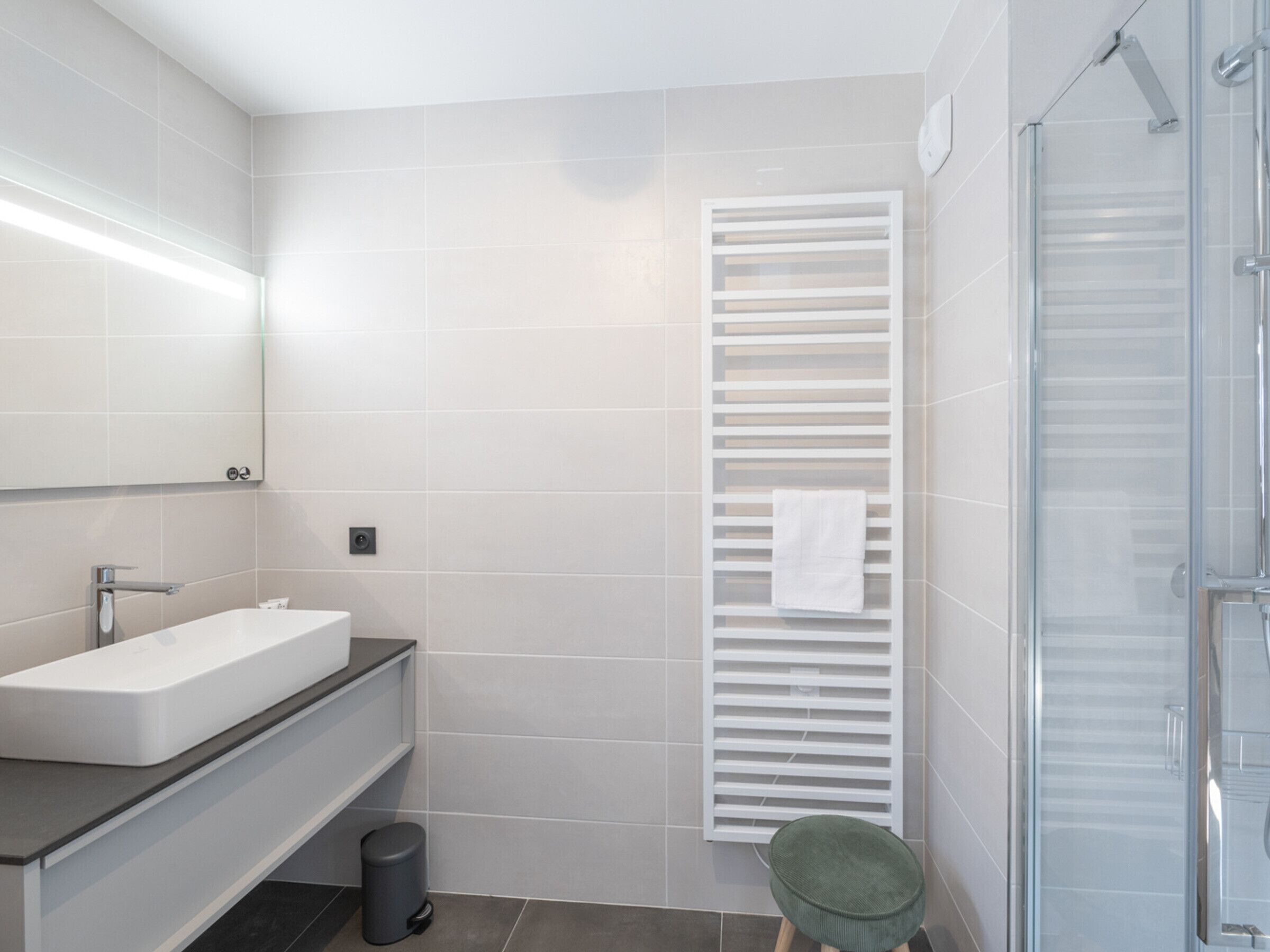 A modern bathroom with a large mirror, a white sink, a towel rack, and a shower area.