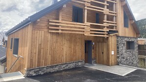 A wooden cabin with a stone foundation, a sloped roof, and a wooden staircase leading to the entrance. - New duplex, near slopes, 8 pax, parking (Huez)