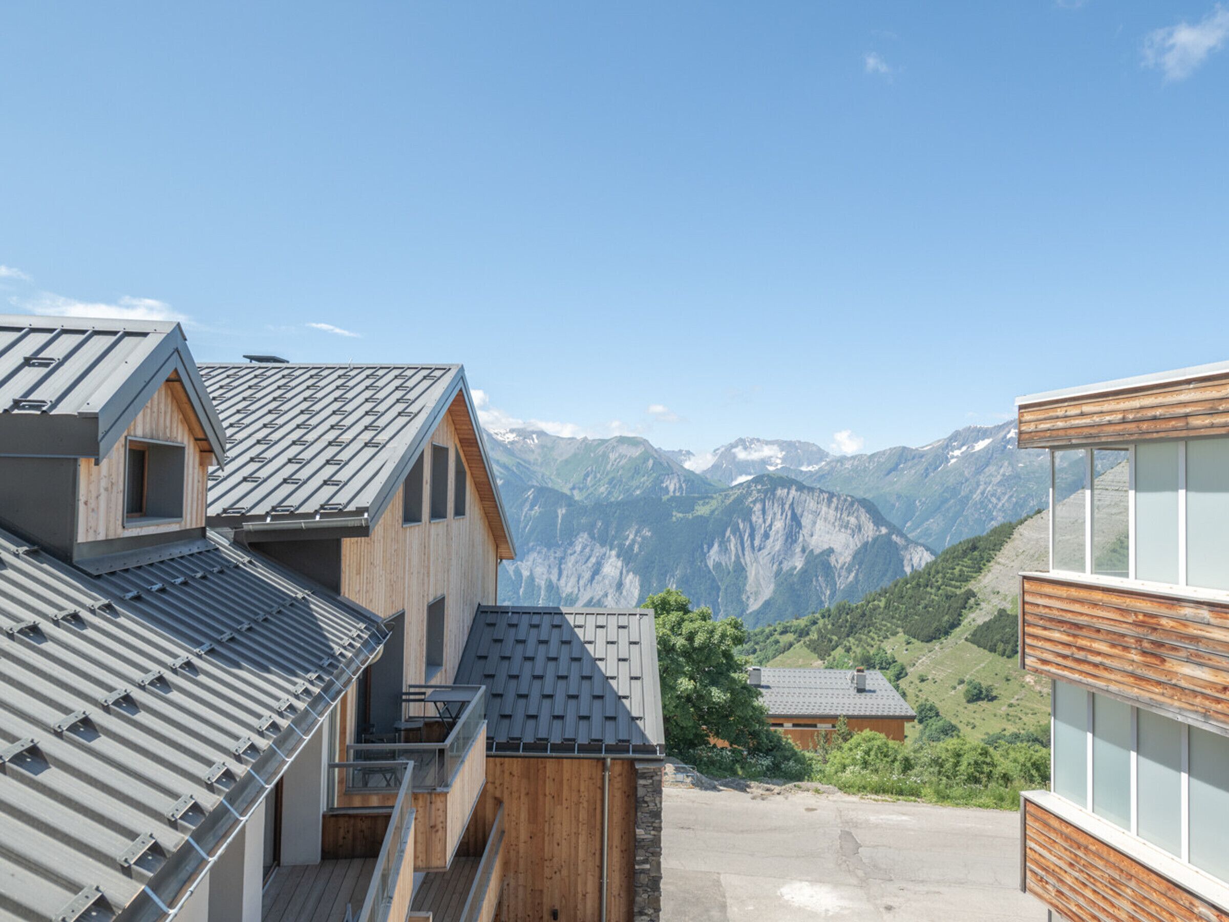 Ein modernes Gebäude mit Satteldach, Holzfassade und Blick auf Berge im Hintergrund.