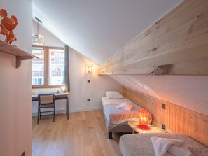 A small, cozy room with a wooden sloped ceiling, a desk with a chair, a bed with a headboard, and a nightstand with a lamp. - New duplex, near slopes, 8 pax, parking (Huez)