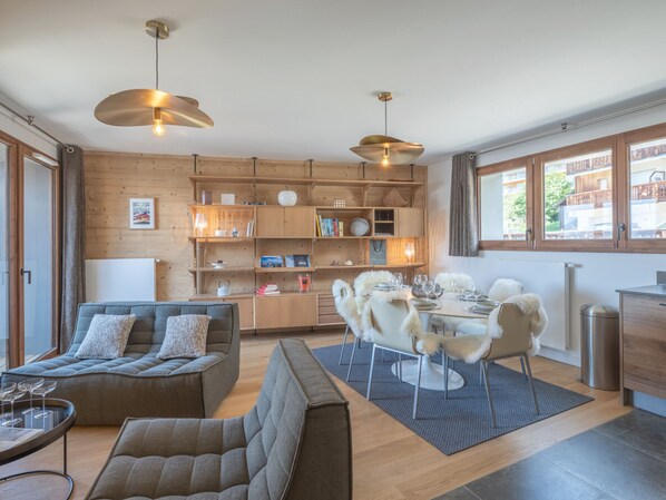 A modern living room with a sofa, a dining table set for four, and a wooden bookshelf. - New duplex, near slopes, 8 pax, parking (Huez)
