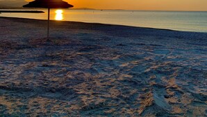 Une scène de plage avec un seul parasol et le soleil se couchant à l’horizon.