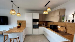 Une cuisine moderne avec des meubles blancs, un îlot central en bois et des luminaires suspendus.