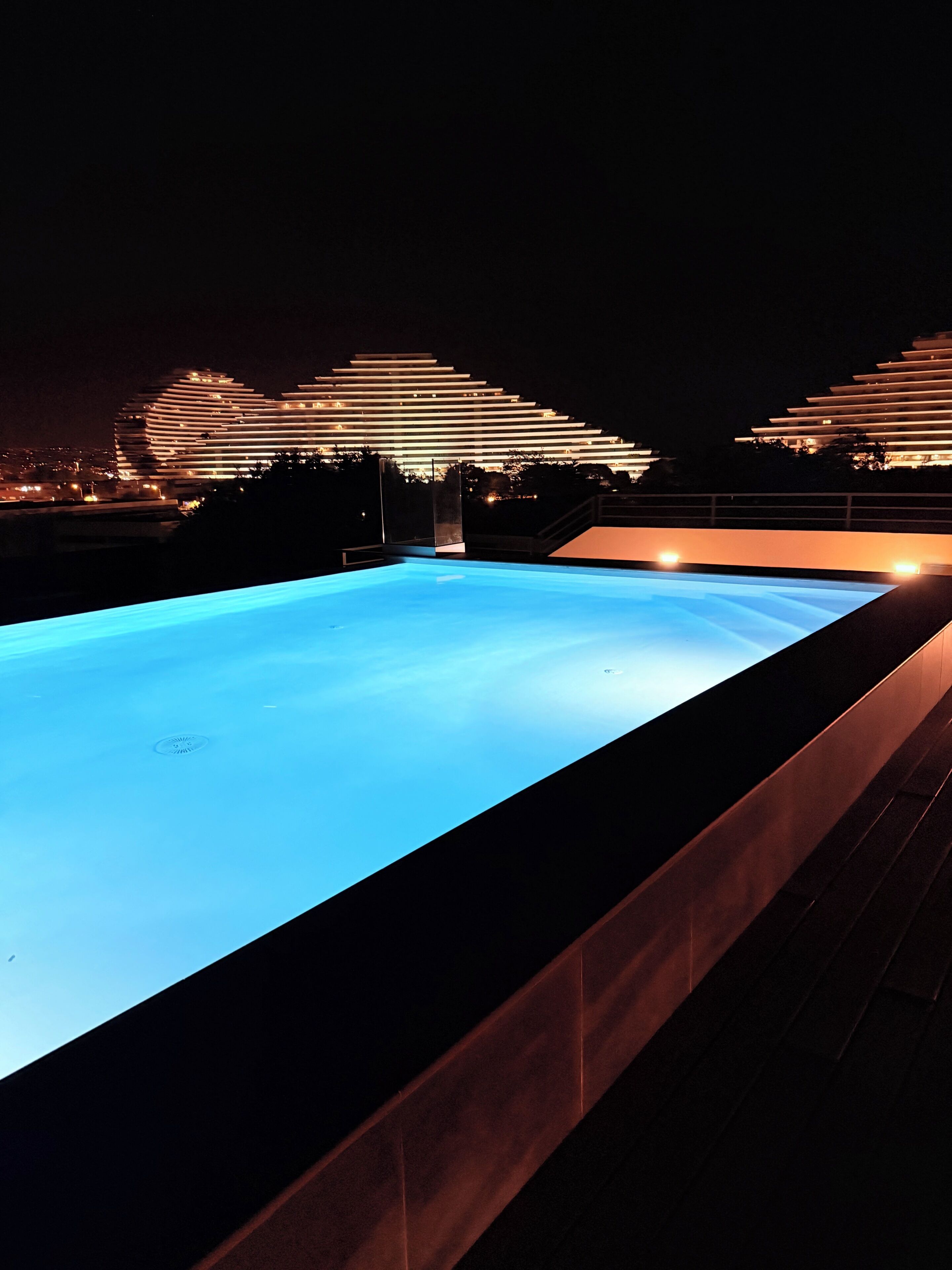 En swimmingpool om natten med en moderne bygning i baggrunden.