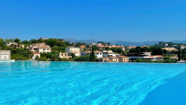 Une piscine d’un bleu éclatant, offrant une vue sur un quartier résidentiel et sur des montagnes lointaines.
