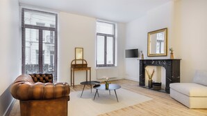 A living room with a leather sofa, a white armchair, a small round table, and a fireplace. - Junior Suite in The Heart of Antwerp (Antwerpen)