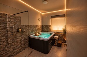 Een moderne badkamer met een stenen muur, een bubbelbad, een douche en een klein tafeltje met handdoeken.