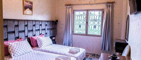 A hotel room with two beds, a TV, a desk, and a window with curtains.