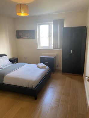 A bedroom with a bed, a nightstand, a dresser, a radiator, and a window with curtains.