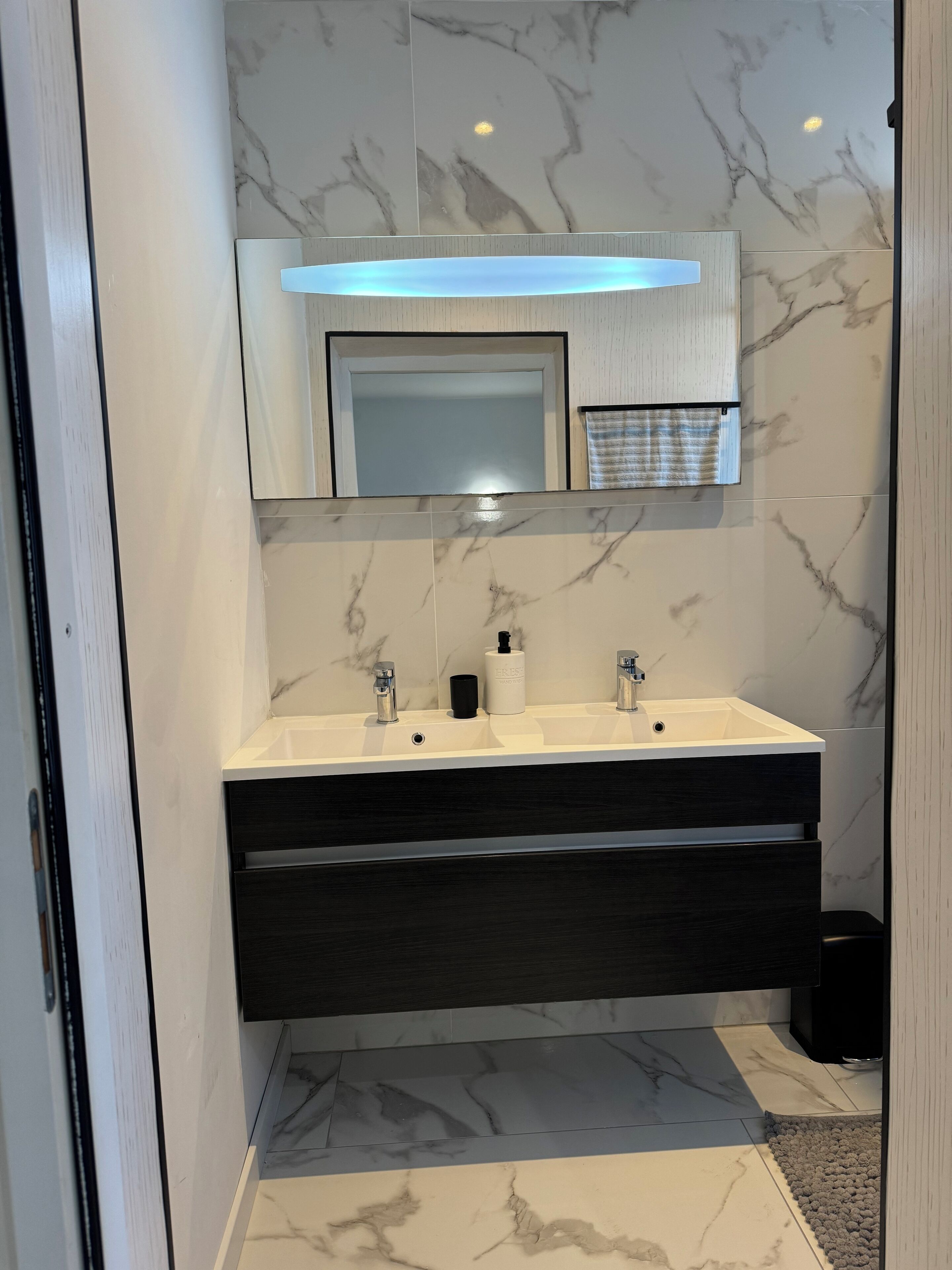 Une salle de bain moderne avec un meuble-lavabo à deux vasques, un pare-feu en marbre et un miroir au-dessus du lavabo.