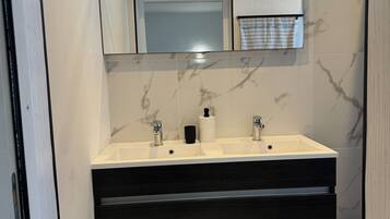 Une salle de bain moderne avec un meuble-lavabo à deux vasques, un pare-feu en marbre et un miroir au-dessus du lavabo.