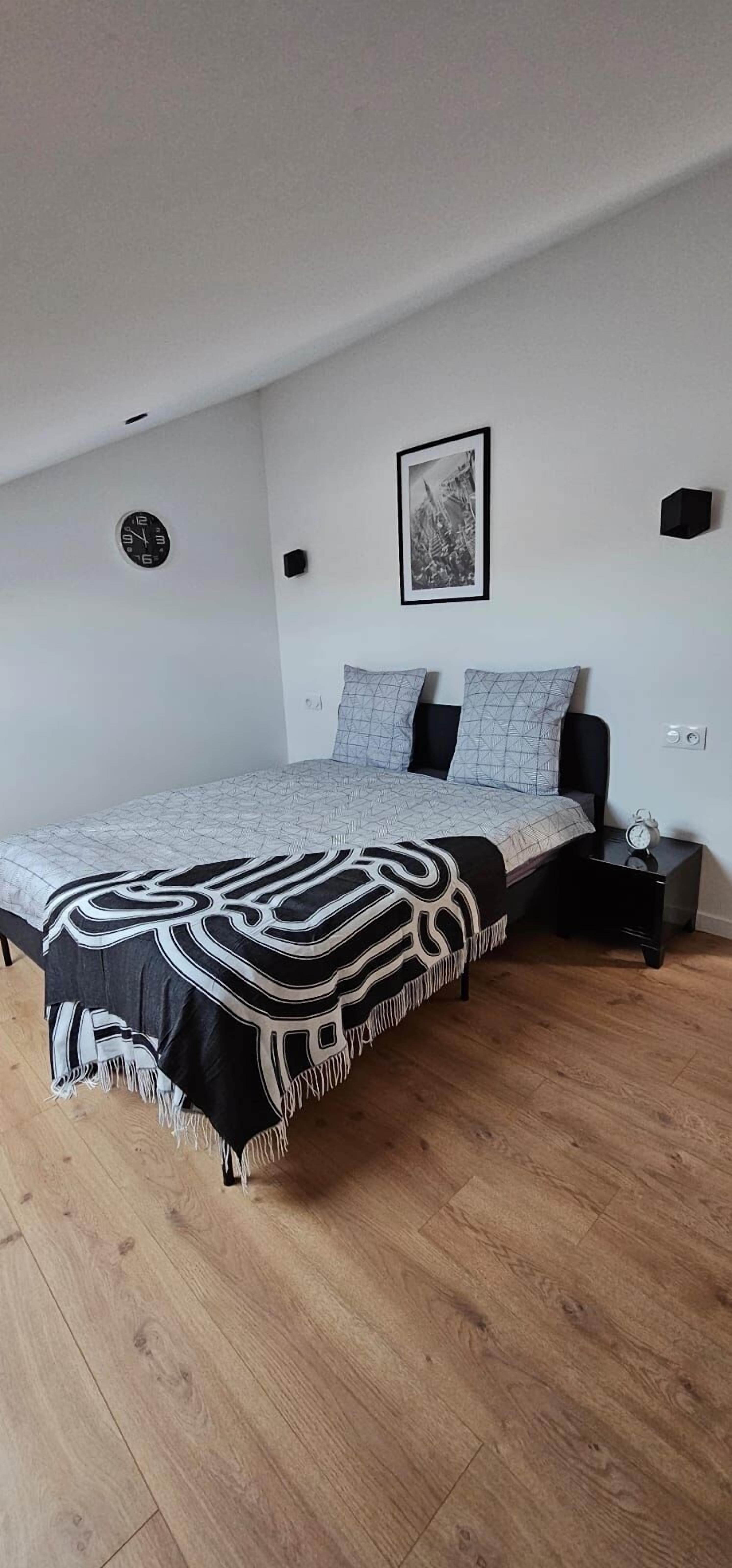 Une chambre à coucher avec un lit, une horloge, un tableau encadré et une table de chevet.
