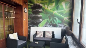 Una habitación con puerta de madera, un reloj de pared, un sofá con cojines estampados, una mesita y un fondo con una pila de rocas y bambú.