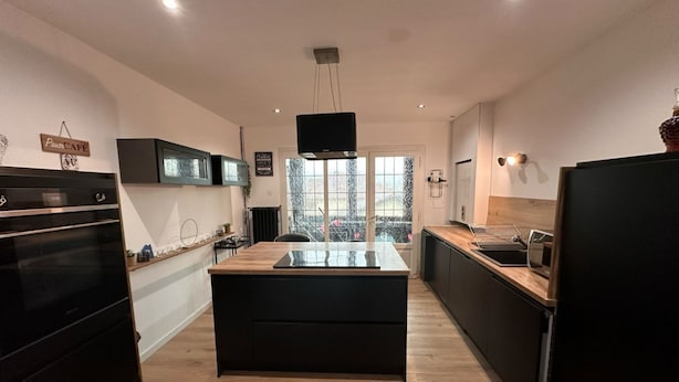 Una cocina moderna con una isla central, armarios oscuros y un amplio ventanal que proporciona luz natural.