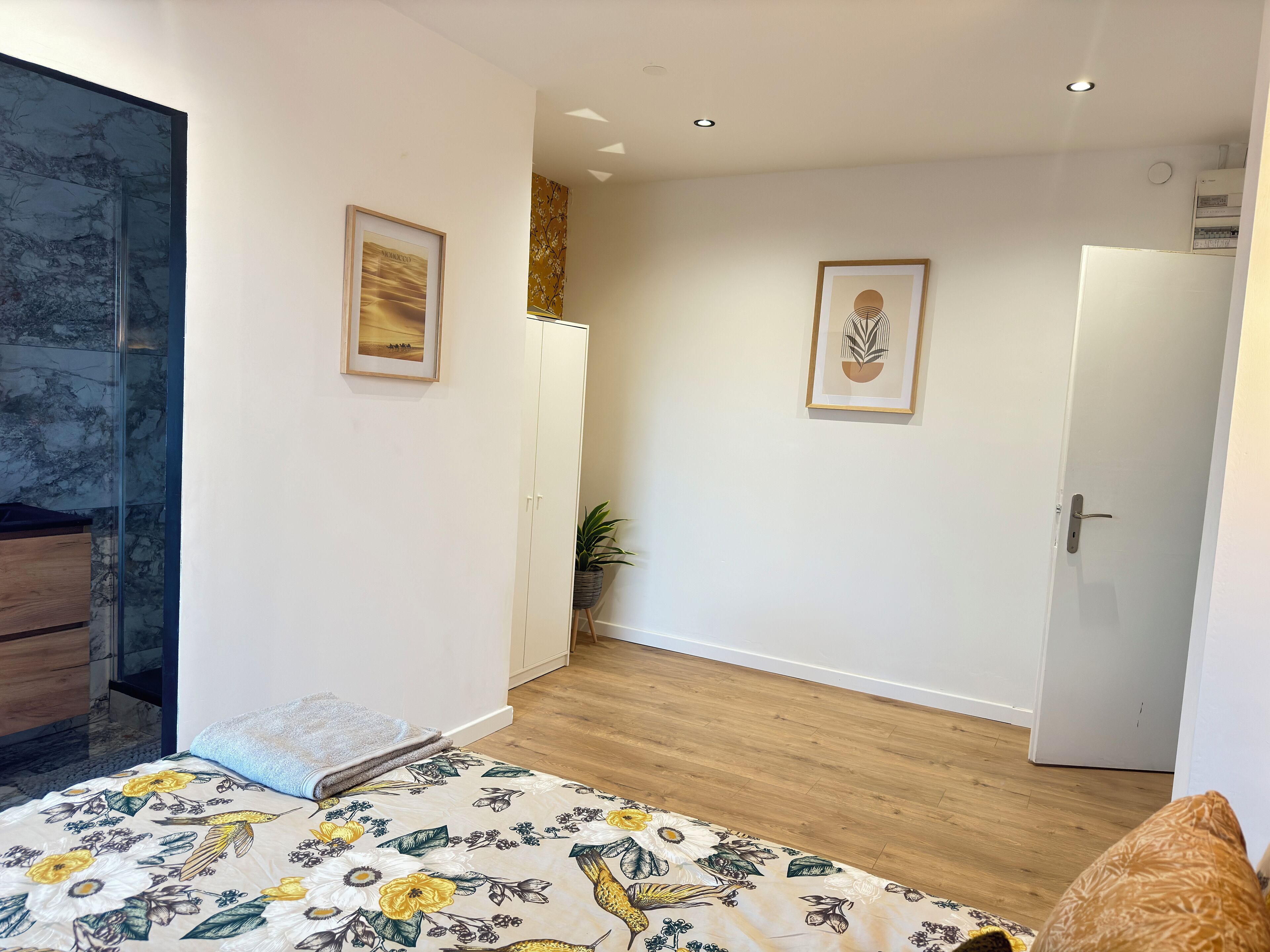 Une chambre à coucher avec un lit, une commode en bois, une armoire blanche, une porte et un tableau encadré au mur.