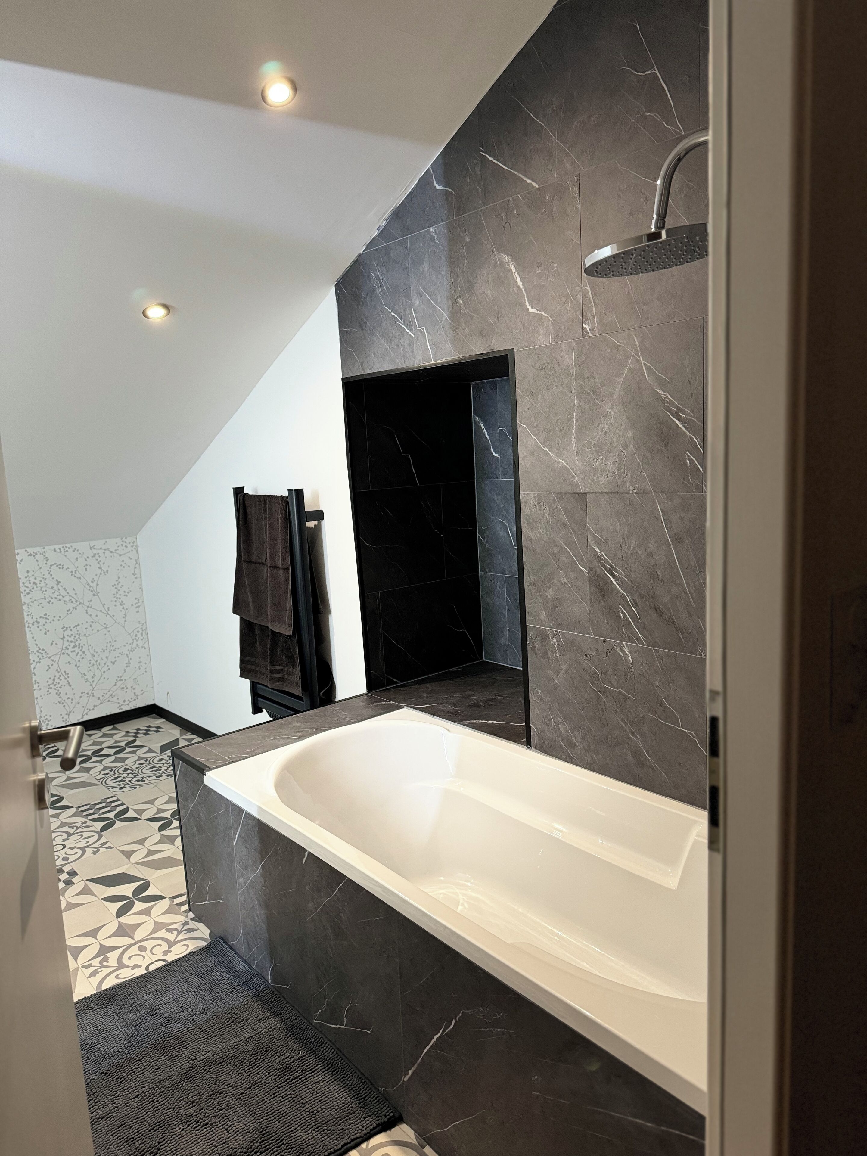 A modern bathroom with a large bathtub, dark marble walls, and a geometric patterned floor.
