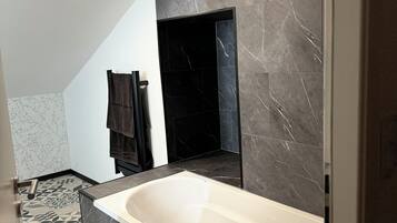 A modern bathroom with a large bathtub, dark marble walls, and a geometric patterned floor.