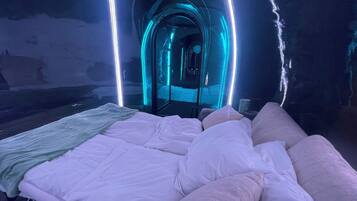A room with a bed, a bench, and a tunnel-like structure with blue lighting.