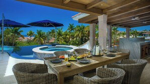 Un espacio de comedor al aire libre con piscina, mobiliario de mimbre y sombrillas.