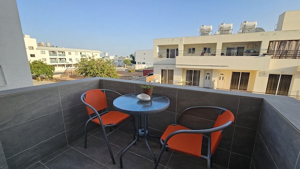 Ein Balkon mit zwei orangefarbenen Stühlen und einem kleinen Tisch, mit Blick auf eine Wohngegend und mehrere Gebäude.