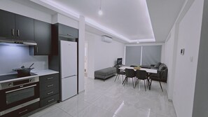 A modern kitchen with a built-in oven, a refrigerator, and a dining area with a table and chairs. - 136 LCA - Stay Aquamarine Apartment (Larnaca)