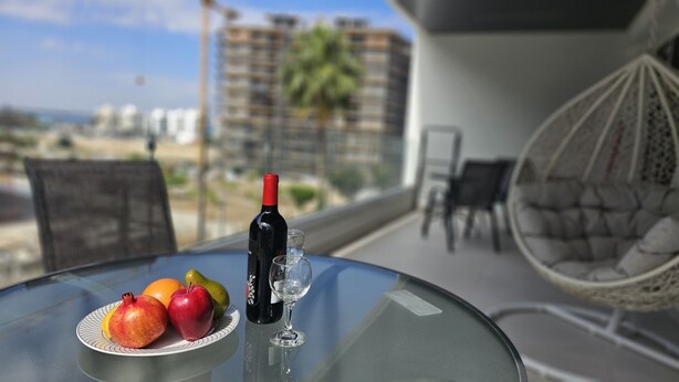 Ein Tisch mit einer Weinflasche, einem Glas und einer Fruchtschale auf einem Balkon mit Blick auf eine Stadtlandschaft.