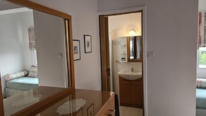 Un baño con lavamanos, espejo y una puerta que da a un dormitorio con cama y ventana.
