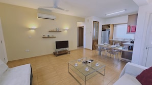 A living room with a TV, coffee table, and dining area with chairs and a table set for four. - 114 PRO - Stay Olivia Apartment (Paralimni)