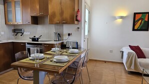 A modern kitchen with wooden cabinets, a dining table set with plates and glasses, a coffee maker, and a toaster. - 114 PRO - Stay Olivia Apartment (Paralimni)