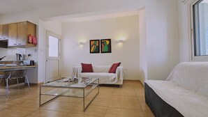 A modern living room with a glass coffee table, a white sofa, and a dining area with a kitchen counter. - 114 PRO - Stay Olivia Apartment (Paralimni)