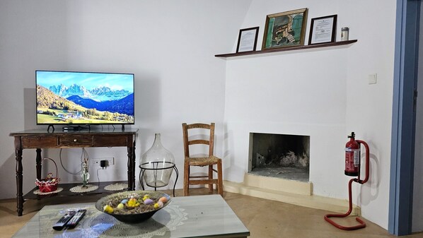 A living room with a television, a fireplace, a chair, a table with a bowl of eggs, and a fire extinguisher. - 133 DRO - Stay Akoni House (Droushia)