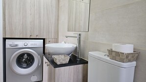 A compact bathroom with a washing machine, a sink, and a toilet.