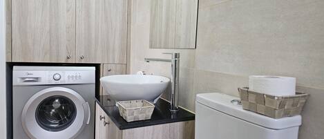 A compact bathroom with a washing machine, a sink, and a toilet.