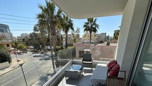 Ein Balkon mit Glasgeländer, einem kleinen Tisch, zwei Stühlen und einem roten Kissen.