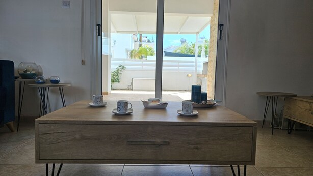 Quarto com uma mesa de madeira posta para o chá, vista para a varanda e um vislumbre do exterior do prédio.