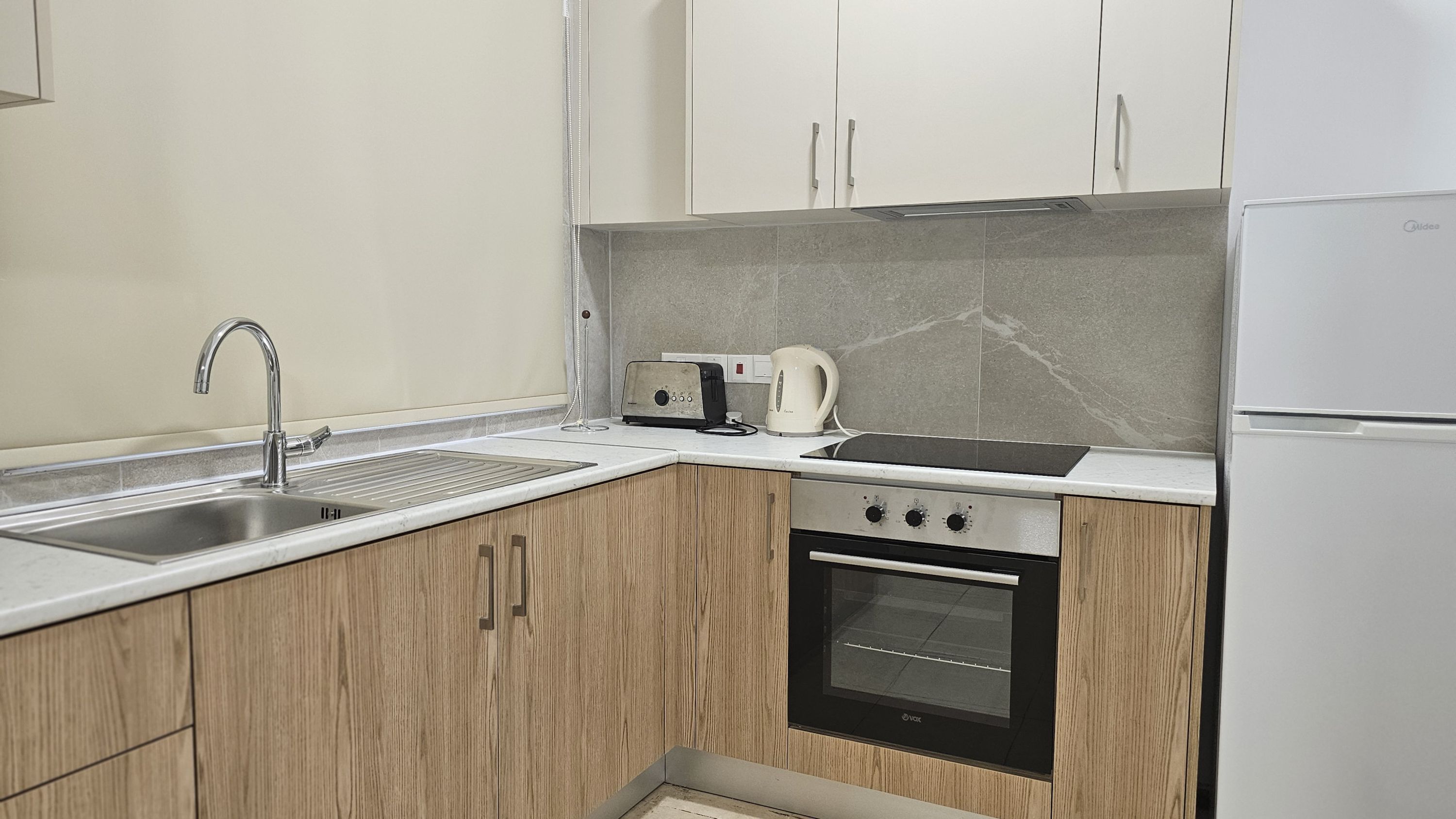 A modern kitchen with a sink, a toaster, a kettle, and a built-in oven.