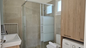 Un baño moderno con cabina de ducha de vidrio, un lavamanos blanco y un mueble de madera.