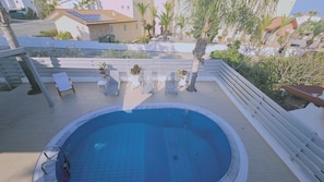 Une piscine sur le toit, avec une terrasse carrelée, entourée de rampes blanches et de plantes en pot.